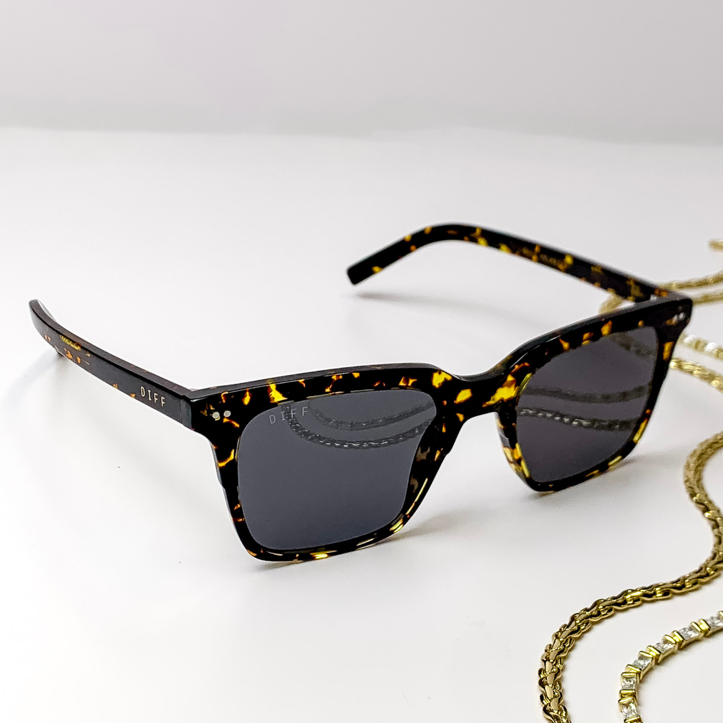 Square black sunglasses with a thick frame, golden yellow spots throughout, and grey lenses