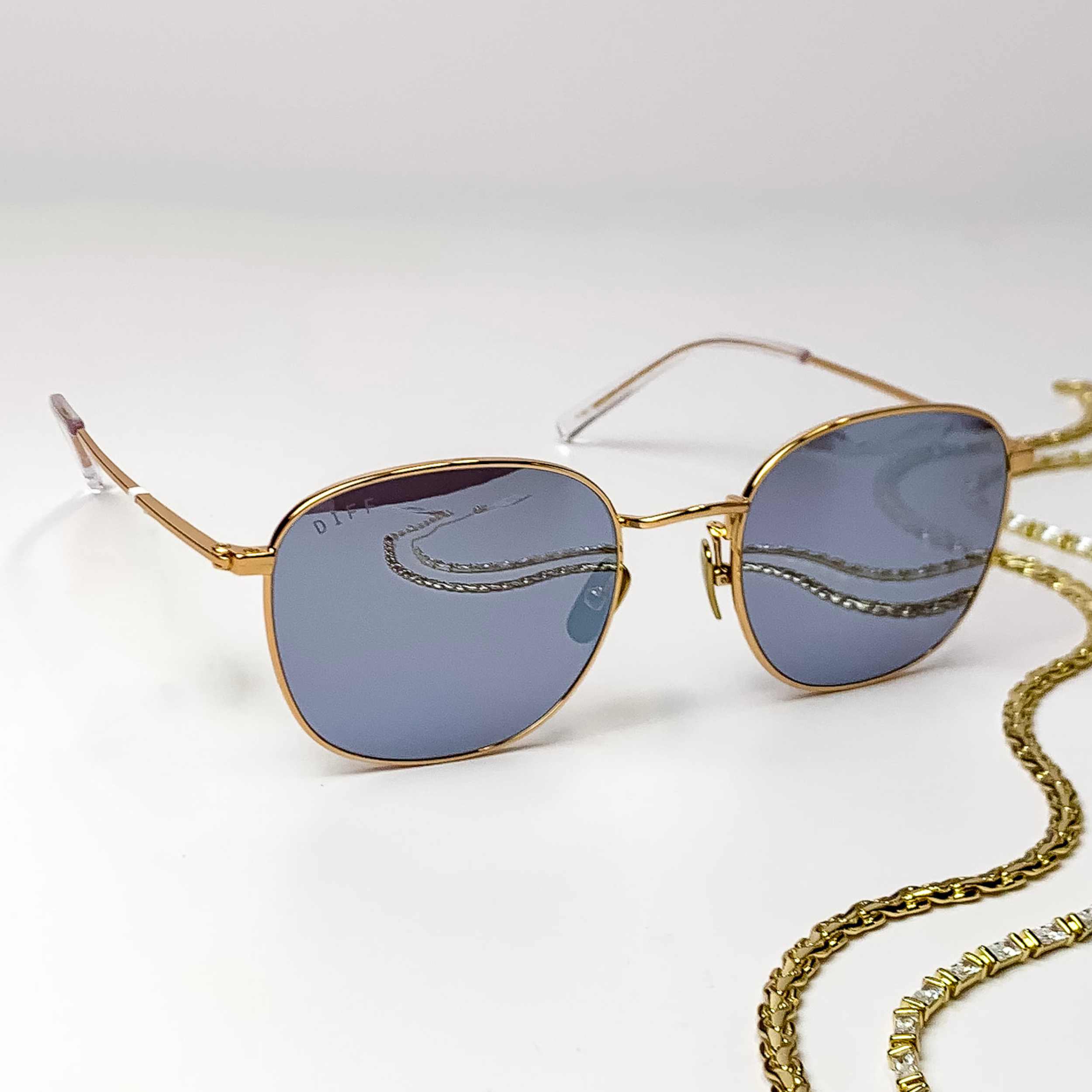 Square gold sunglasses with a thin frame, clear ear tips, and grey lenses