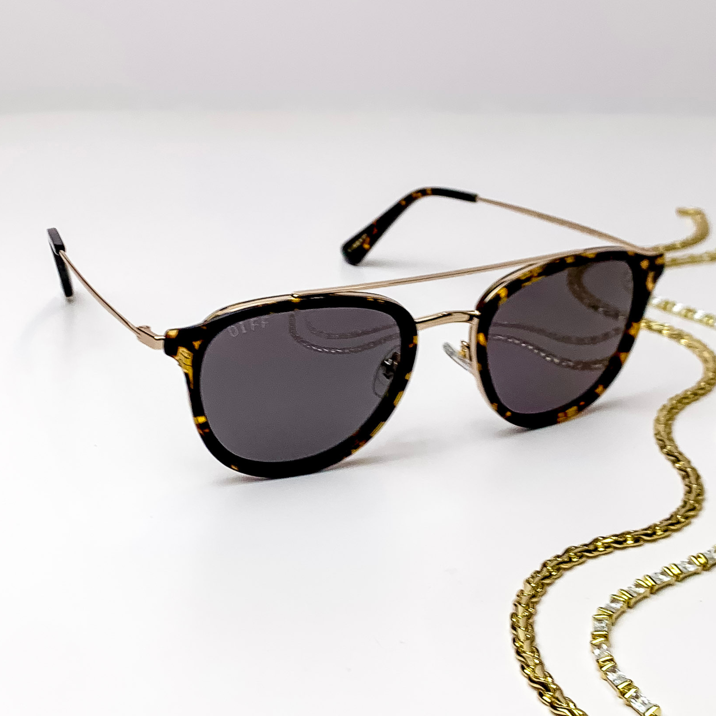 Aviator style gold glasses featuring a black frame with golden yellow spots and matching end pieces. Also features grey polarized lenses. 