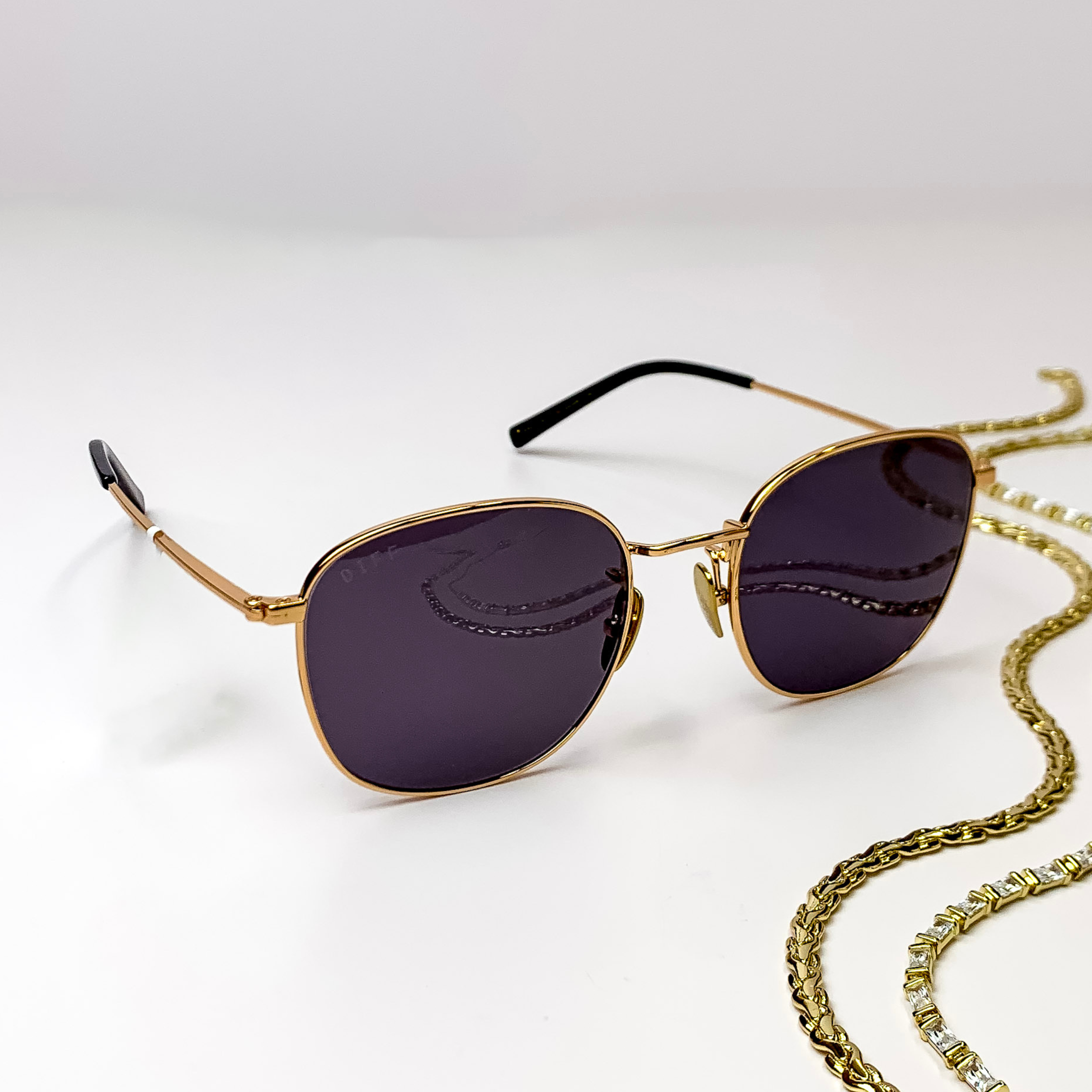 Square gold sunglasses with a thin frame, black ear tips, and grey lenses.