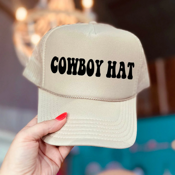 In the picture is a foam trucker hat with the words cowboy hat across the top in a cream color with a white background.