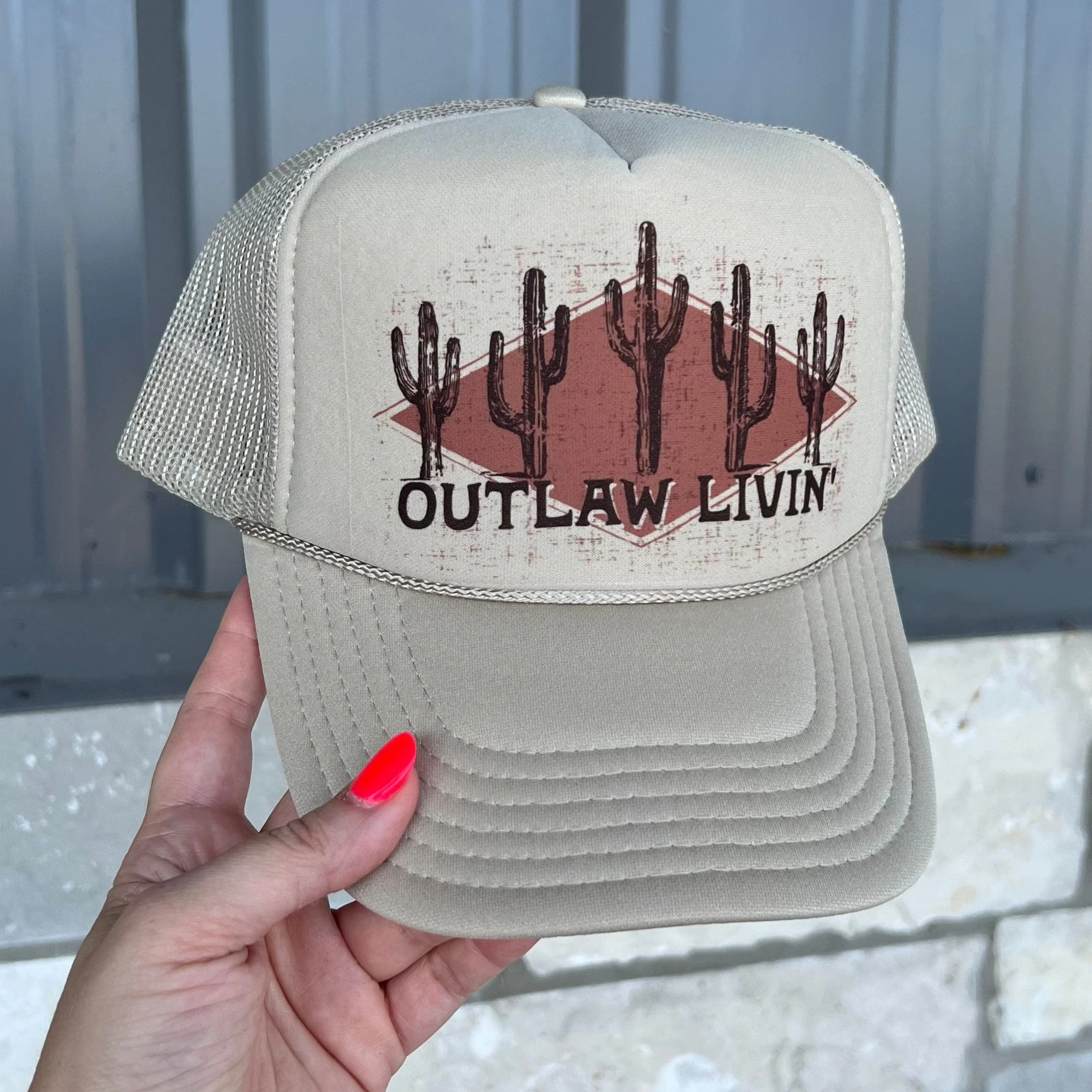 In the picture is a foam trucker hat that has cactus on it with the saying outlaw livin across the top 