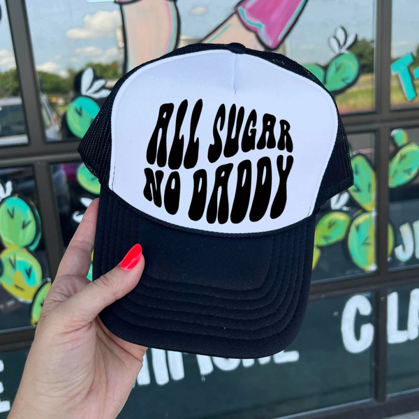 In the picture is a trucker hat that says all sugar no daddy across the top in black and white