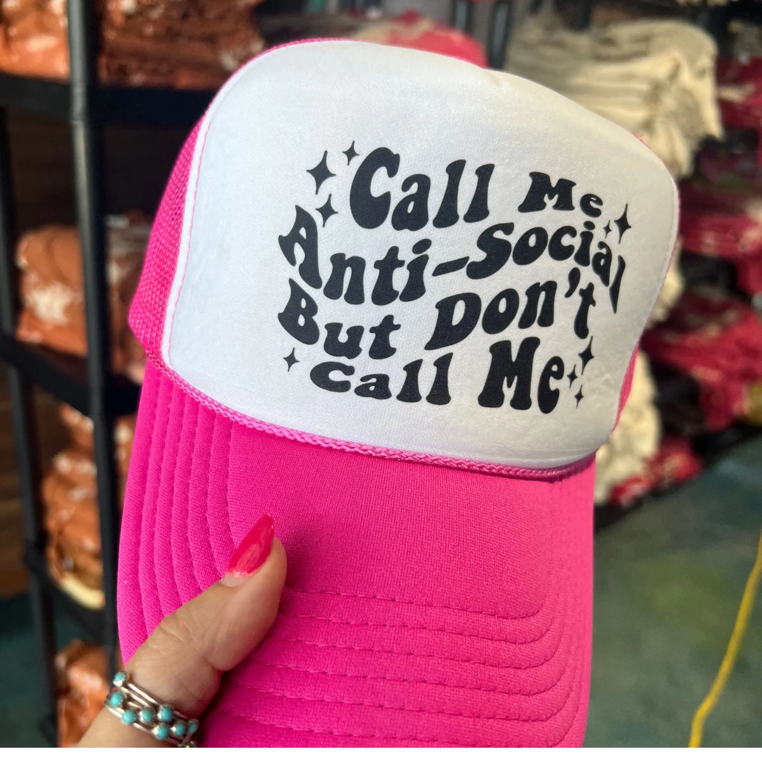 In the picture is a foam trucker hat that says call me anti-social but don't call me across the top in pink and white