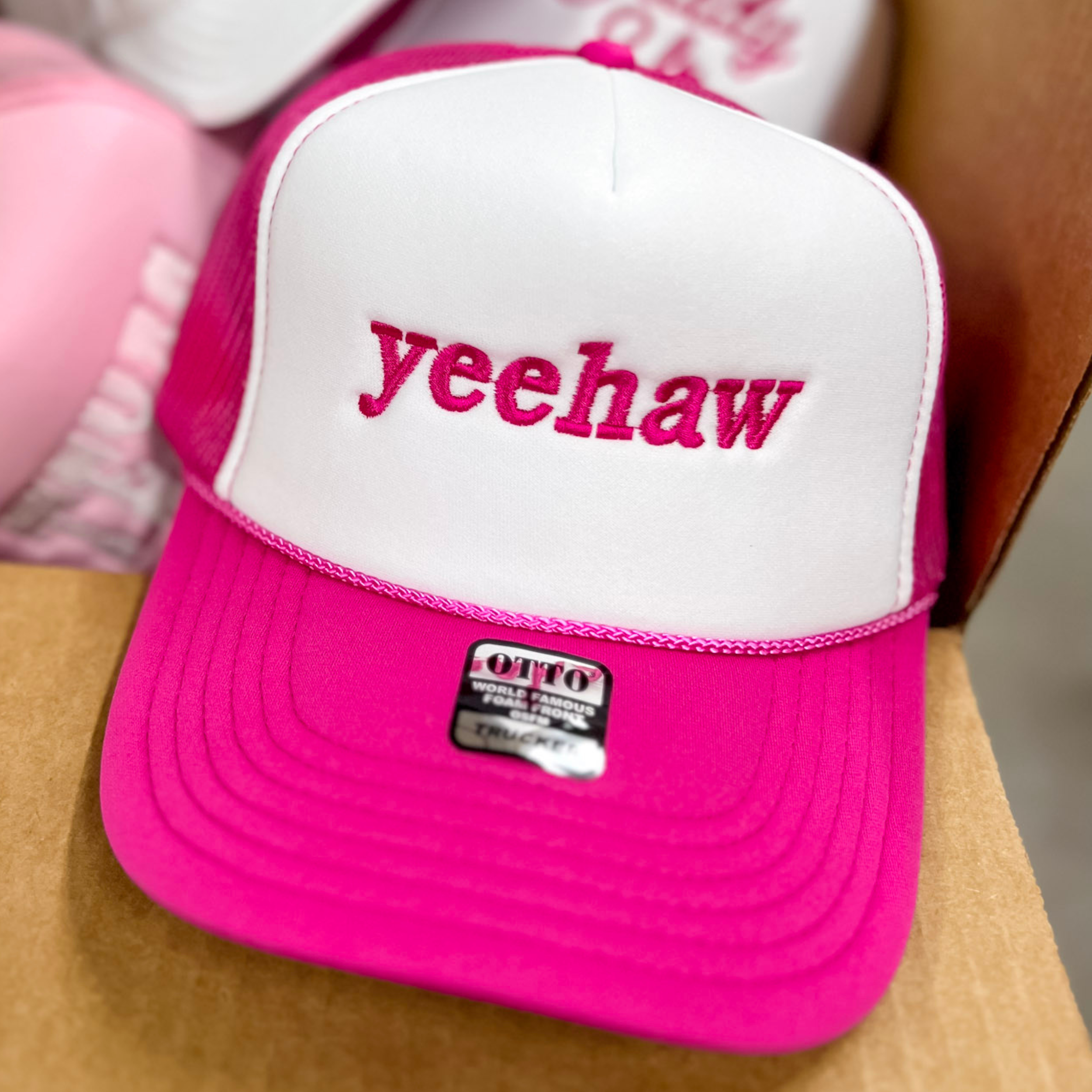 Photo pictures a hot pink and white trucker hat featuring hot pink embroidery of the word Yeehaw.