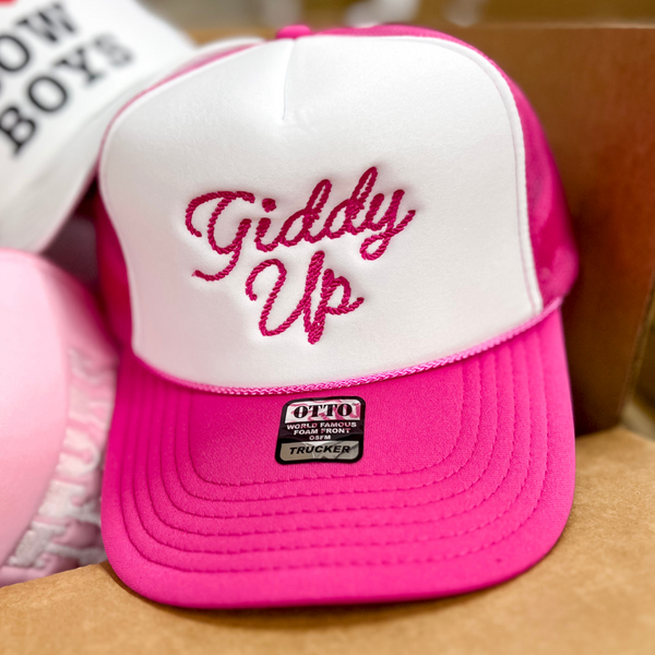 Photo features a hot pink and white trucker hat with pink cursive embroidery of the words giddy up on the front.