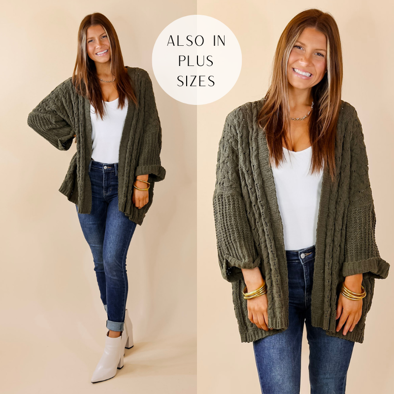 Model is wearing an olive green cardigan with a cable knit materal and an open front. Model has paired the cardigan with a white top, skinny jeans, white booties, and gold tone jewelry. 