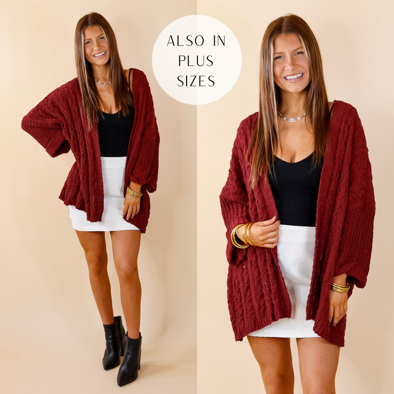 Model is wearing a maroon cardigan with a cable knit material and an open front. Model has paired the cardigan with a black top, white skirt, black booties, and gold tone jewelry. 