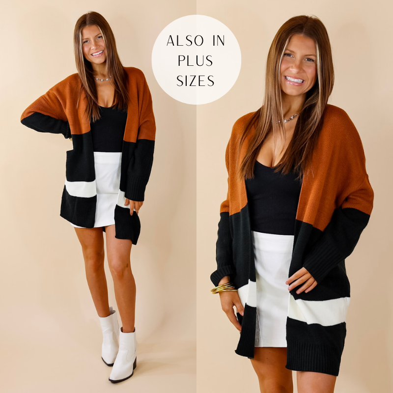 Model is wearing a cardigan with color blocks of rust brown, black, and white. Model has paired the cardigan with a black top, white skirt, white booties, and gold tone jewelry.