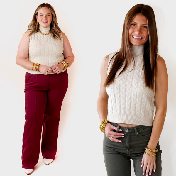 Model is wearing a sleeveless ivory cropped sweater with a high neckline. Model has paired the sweater with olive green pants, beige booties, and gold tone jewelry.