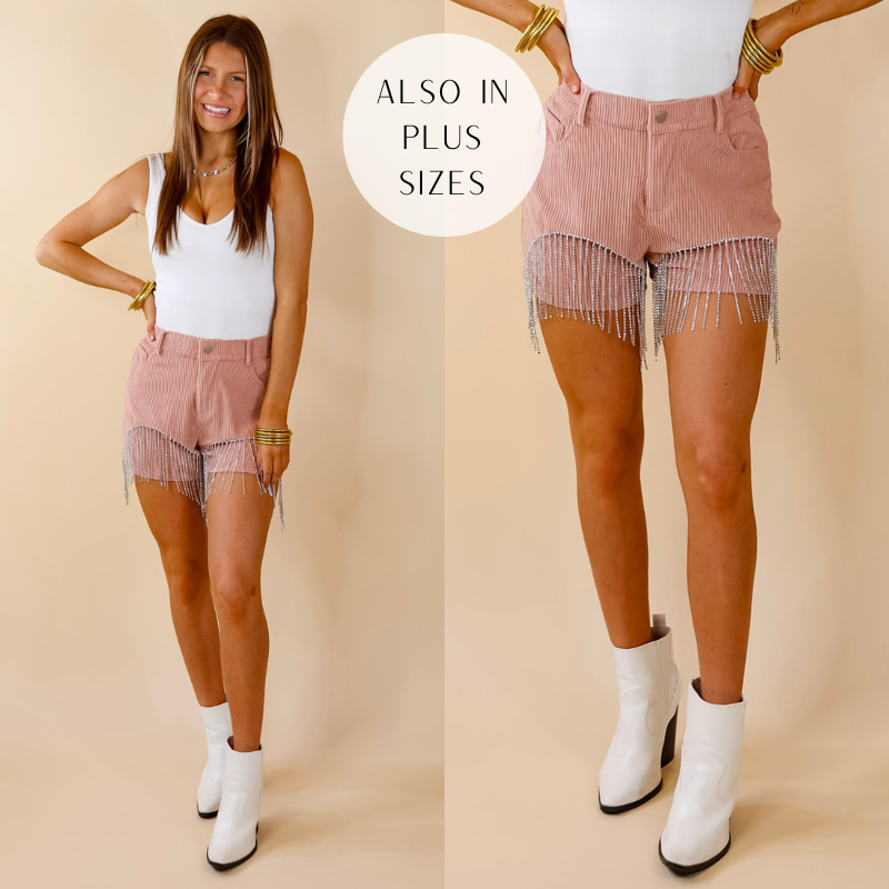 Model is wearing mauve pink corduroy shorts with crystal fringe. Model has paired the shorts with a white bodysuit, white booties, and gold tone jewelry. 