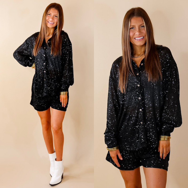 Model is wearing a long sleeve black sequin button up top. Model has paired the top with matching black sequin shorts, white booties, and gold tone jewelry. 