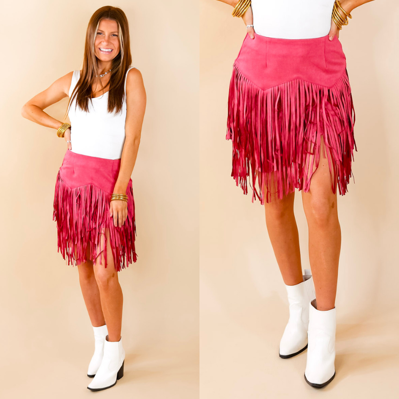 Model is wearing a pink skirt with fringe in a zig zap pattern. Model has paired the skirt with a white bodysuit, white booties, and gold tone jewelry. 