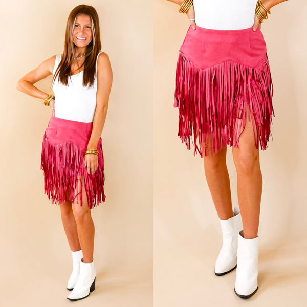 Model is wearing a pink skirt with fringe in a zig zap pattern. Model has paired the skirt with a white bodysuit, white booties, and gold tone jewelry. 