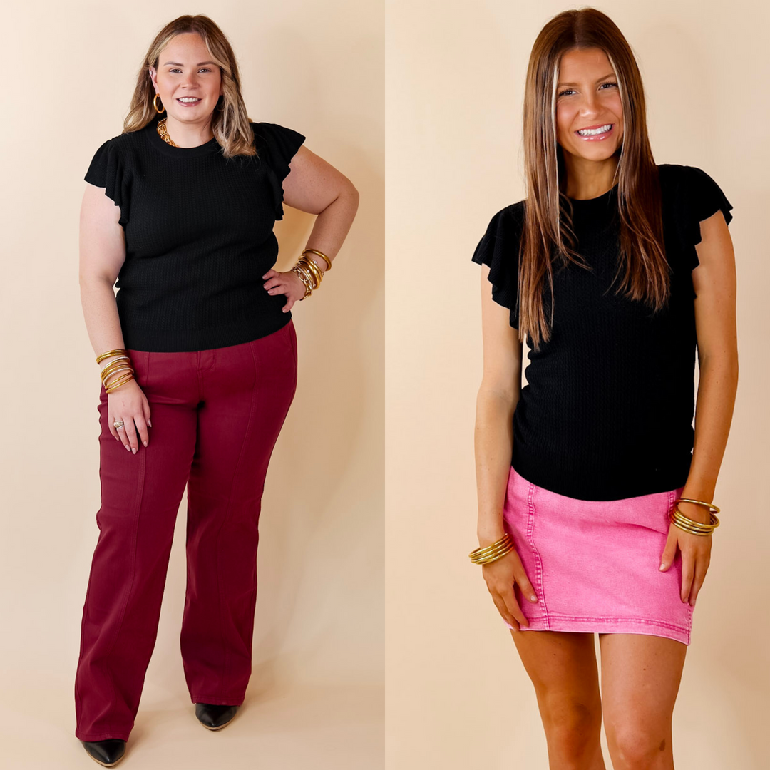 Model is wearing a black ruffle sleeves sweater top. Model has paired the top with burgundy pants, black booties, and gold tone jewelry.