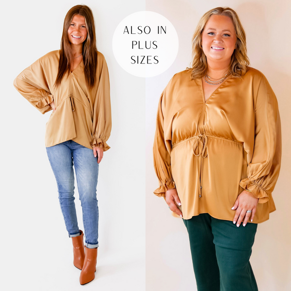 Model is wearing a gold long sleeve top featuring a V neckline, puffed sleeves, tie waist, and flowy body.