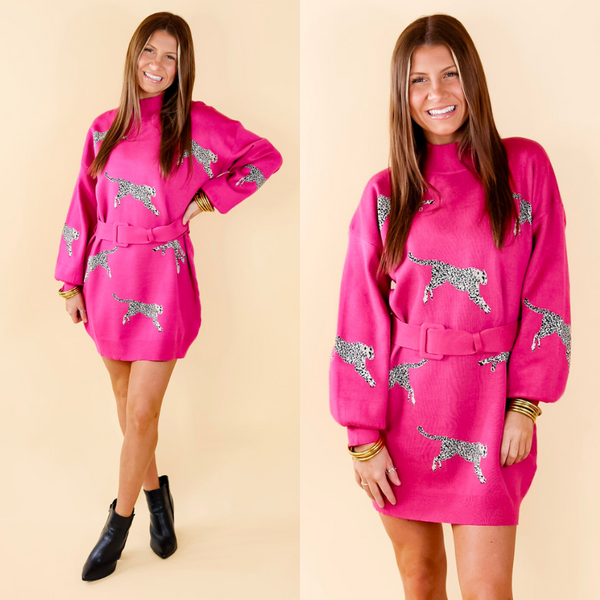 Model is wearing a hot pink sweater dress with belt that has a print of leopards on it. Model has paired the dress with black booties and gold tone jewelry. 