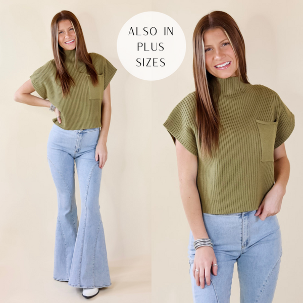 Model is wearing an olive green sweater top with a mock neckline and a front pocket. Model has paired the top with light washed bell bottoms, white booties, and silver tone jewelry. 