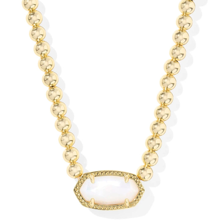A solid white background with a gold beaded necklace and a pendant with kendra scott's signature sone in Ivory mother of pearl.