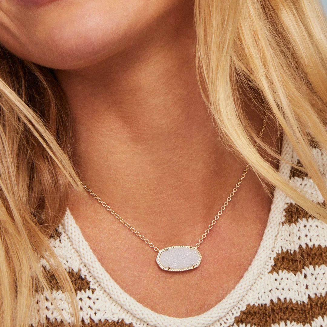 Woman wearing a gold necklace with a iridescent drusy pendant against a blurred background