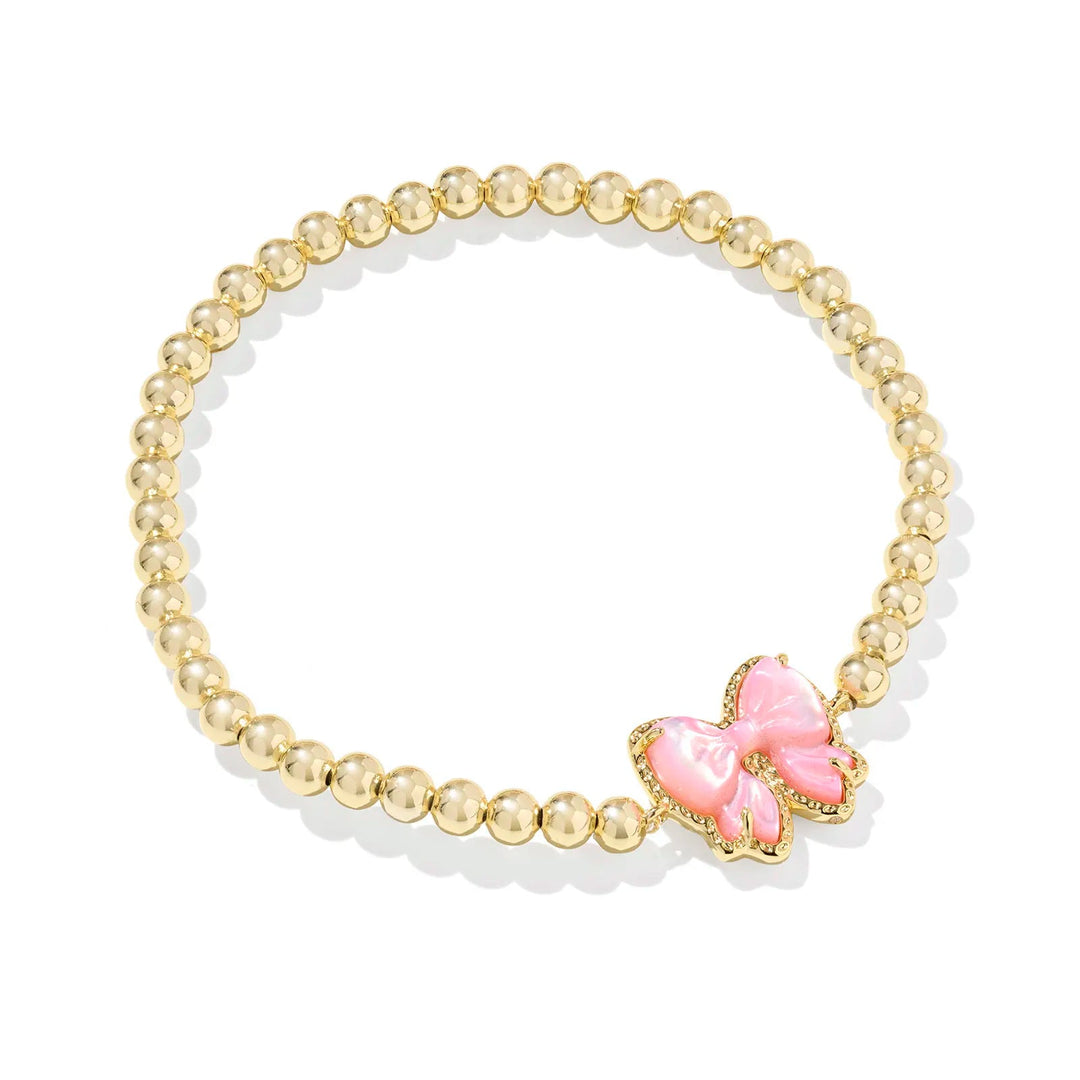 Gold beaded bracelet with a pink bow charm on a white background