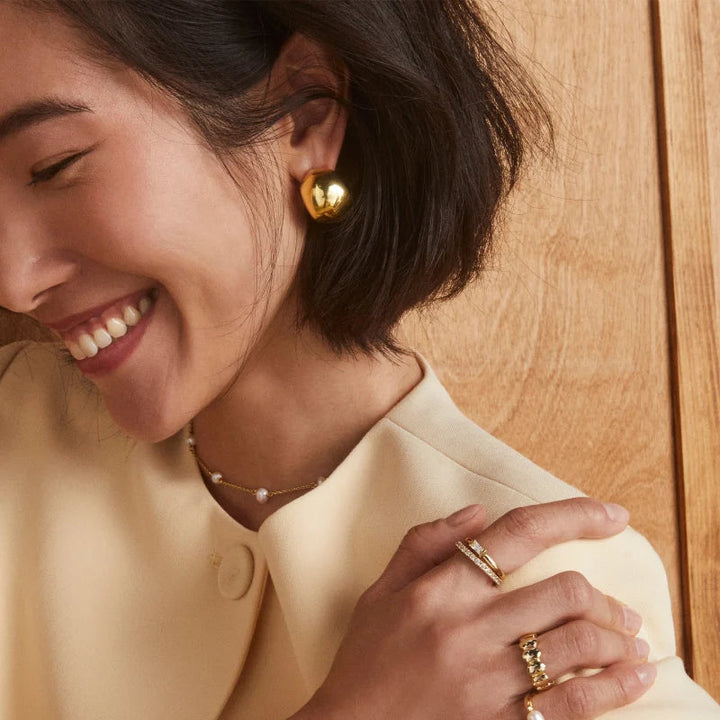 Woman wearing gold earrings, rings, and a bracelet on a wooden background
