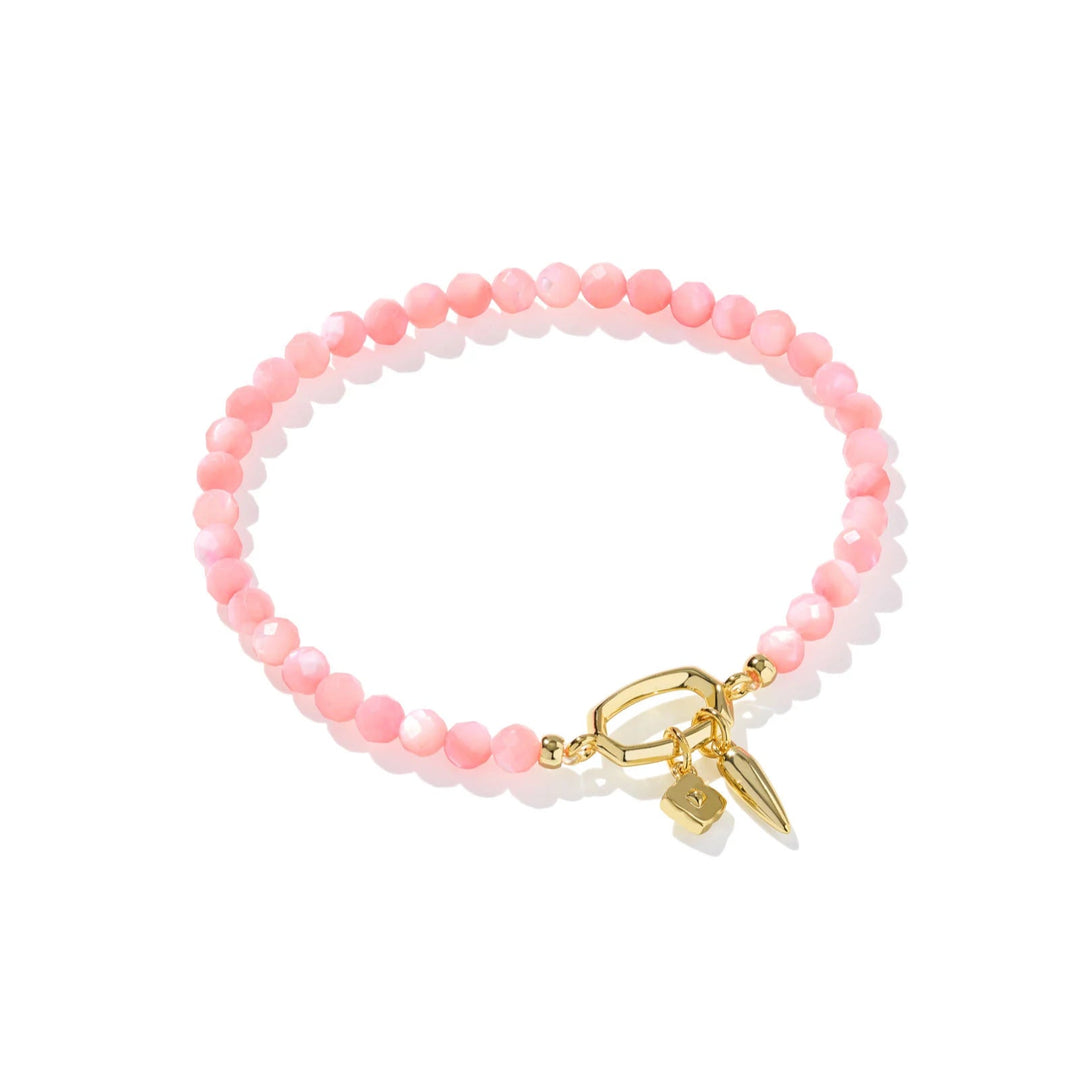 A solid white background with a pink beaded bracelet by kendra scott with a gold toggle closure.