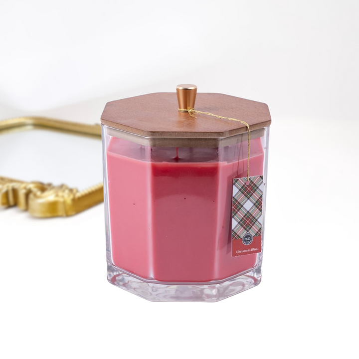 A solid white background with a gold mirror and a large candle in the front, The glass candle has a wooden with with a gold handle.