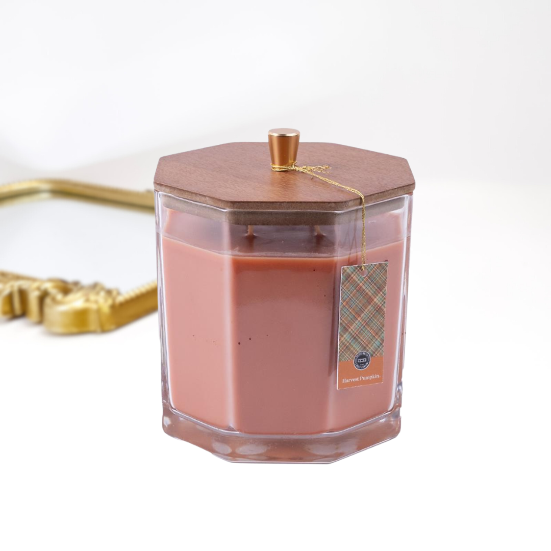 A solid white background with a gold mirror and a large candle in the front, The glass candle has a wooden with with a gold handle.