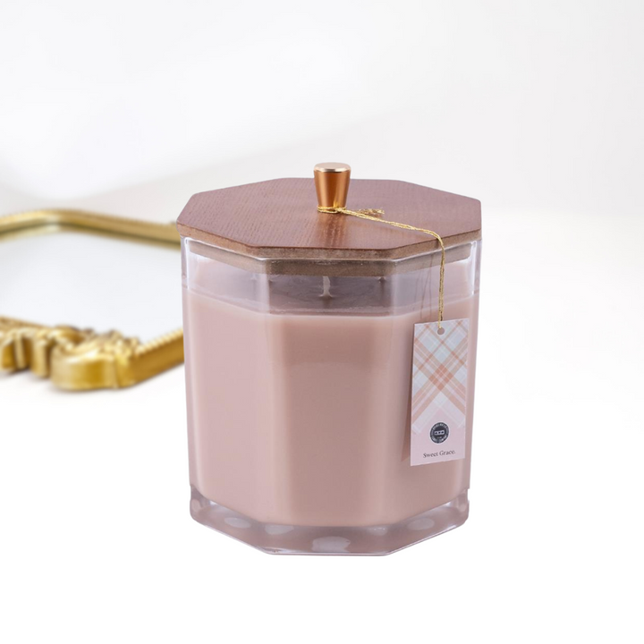 A solid white background with a gold mirror and a large candle in the front, The glass candle has a wooden with with a gold handle.