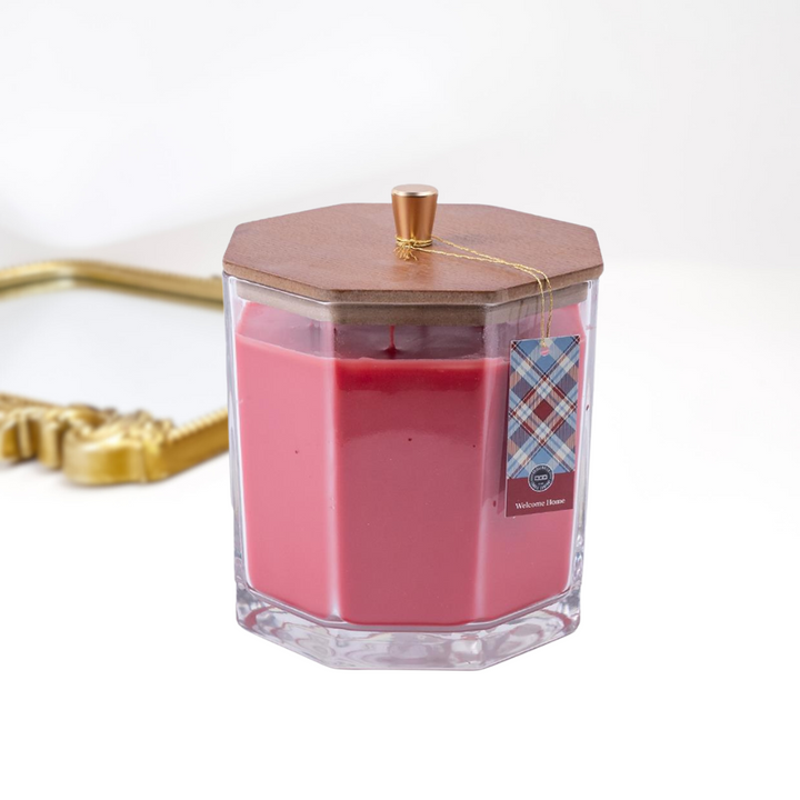 A solid white background with a gold mirror and a large candle in the front, The glass candle has a wooden with with a gold handle.