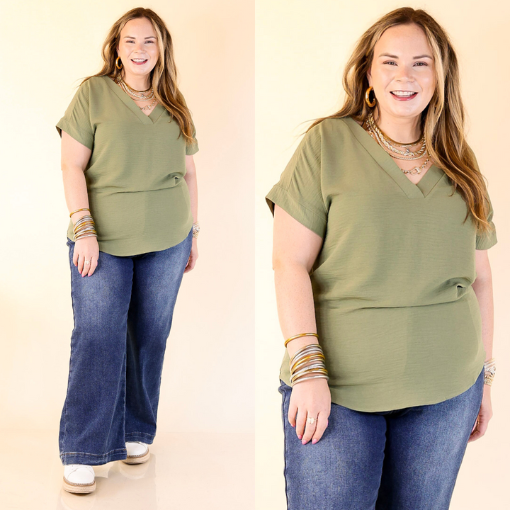 Woman wearing an olive green top and blue jeans on a beige background.