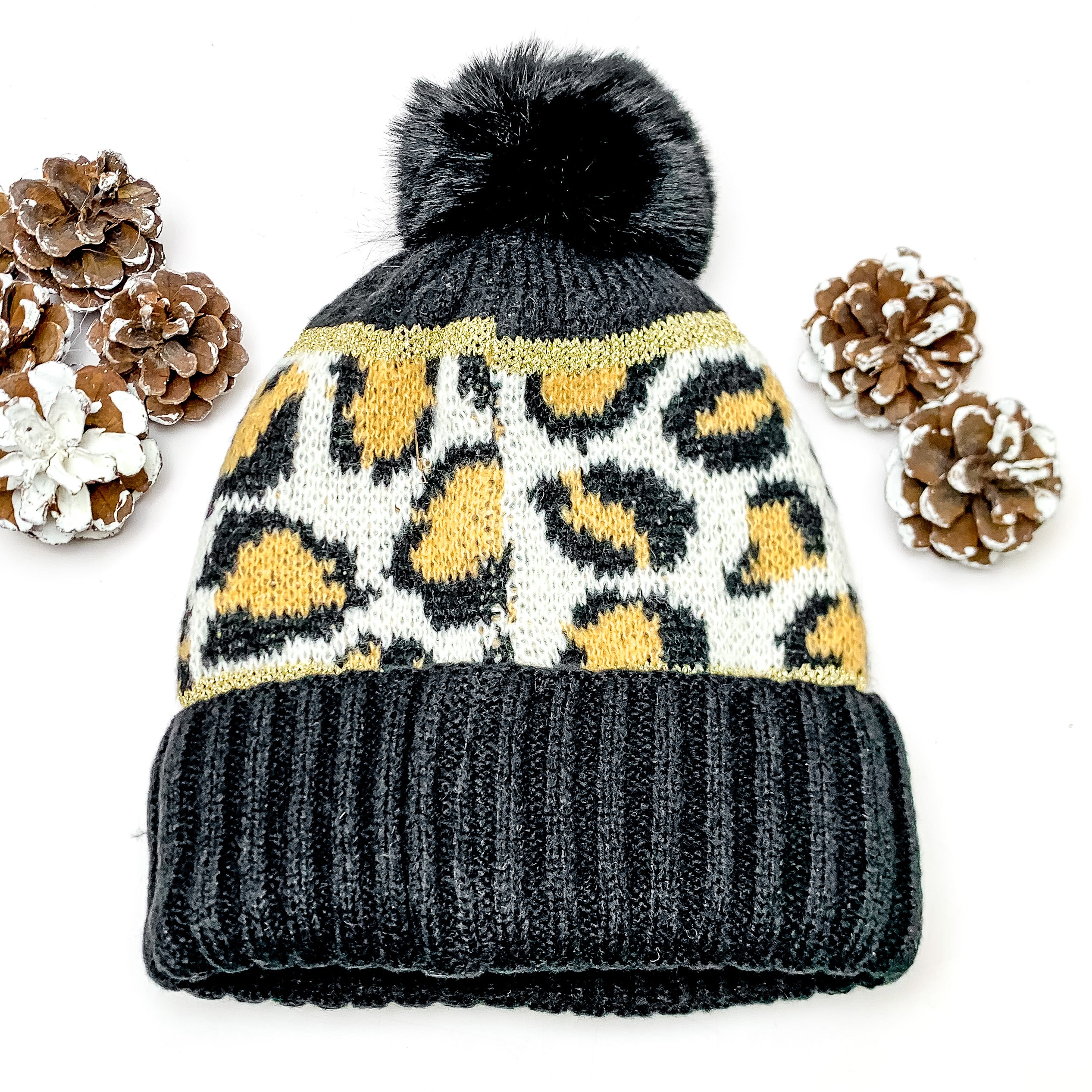 Lucky Leopard Beanie in Black and Brown. This beanie is pictured on a white background with pinecones surrounding it.