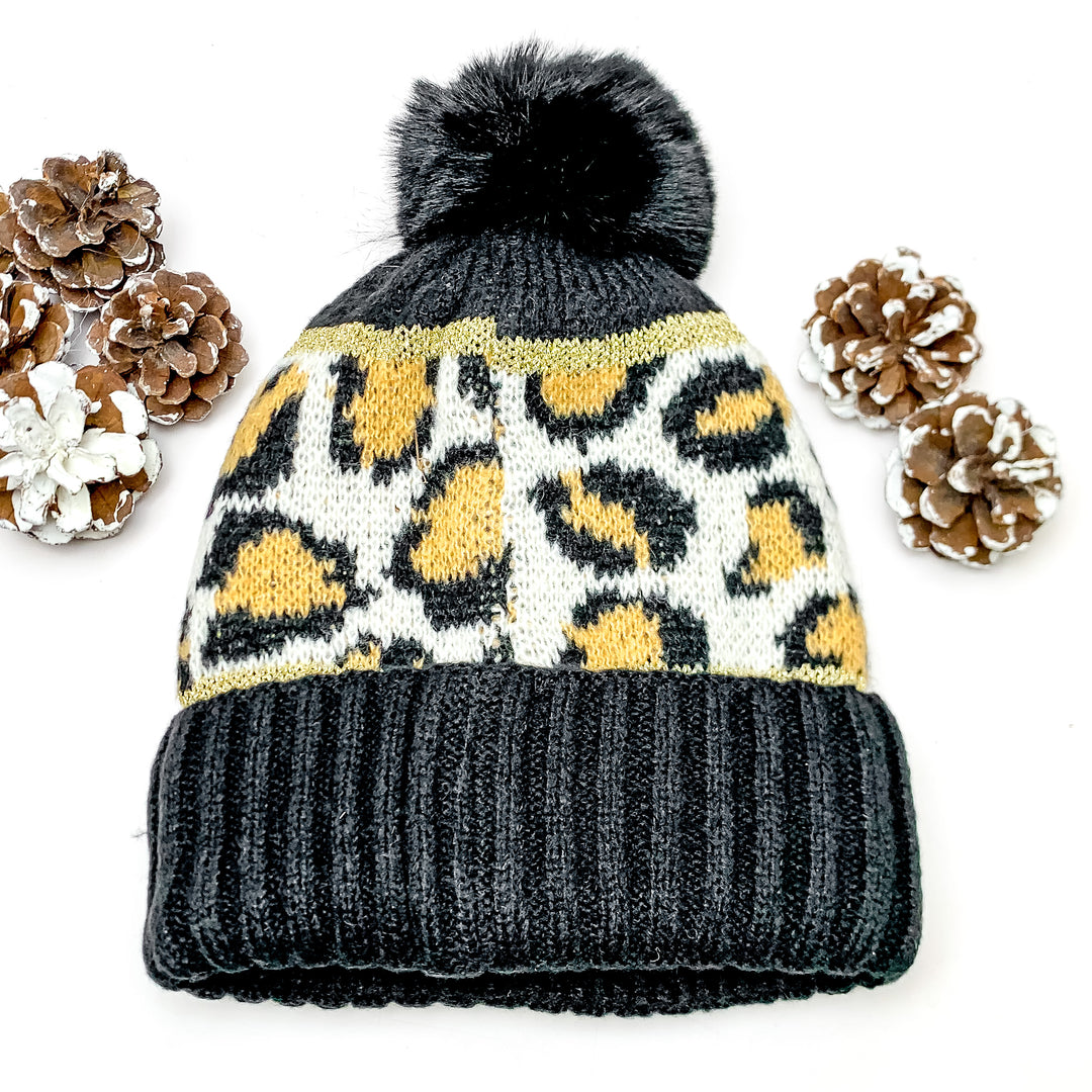 Lucky Leopard Beanie in Black and Brown. This beanie is pictured on a white background with pinecones surrounding it.