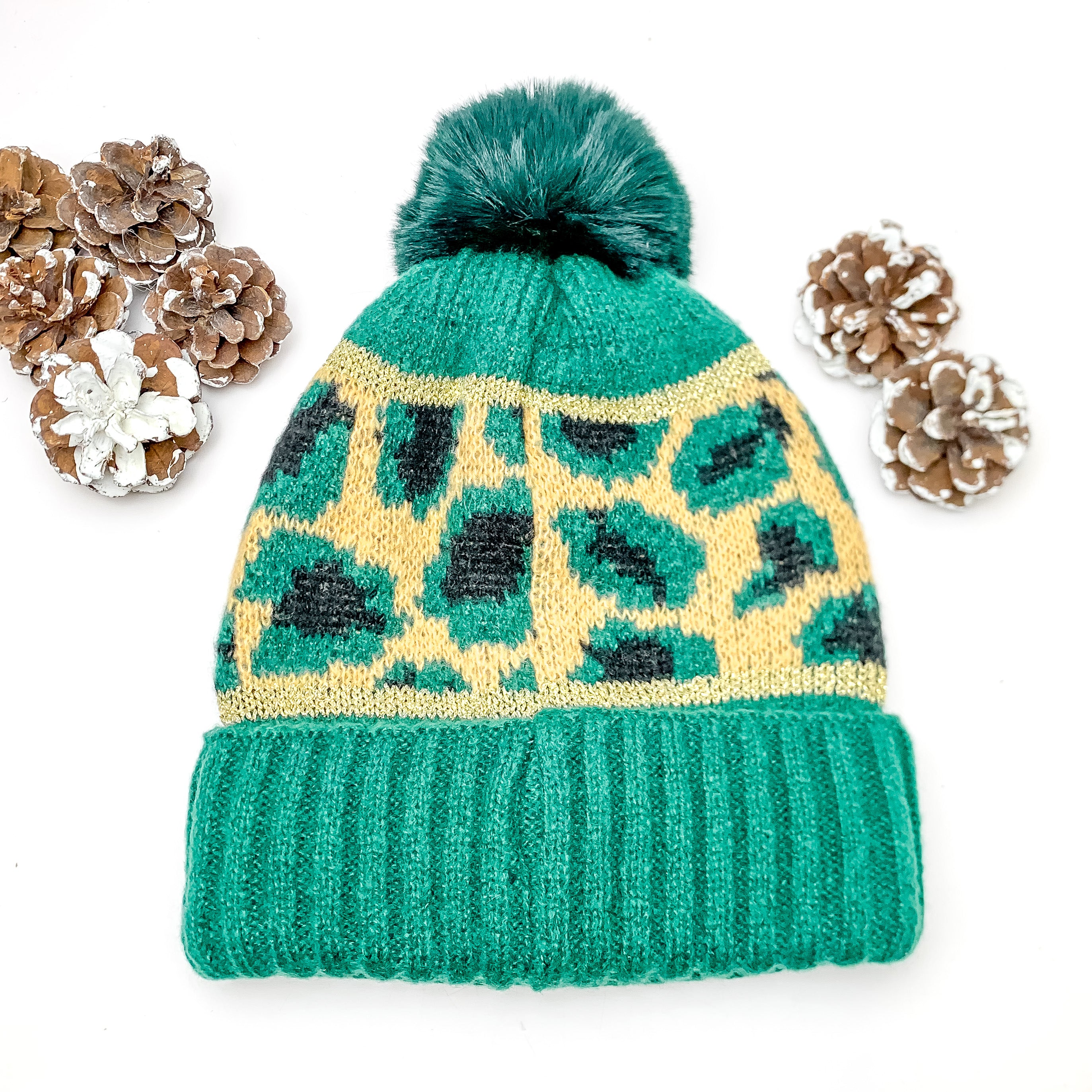 Lucky Leopard Beanie in Forest Green and Beige. This beanie is pictured on a white background with pinecones surrounding it.