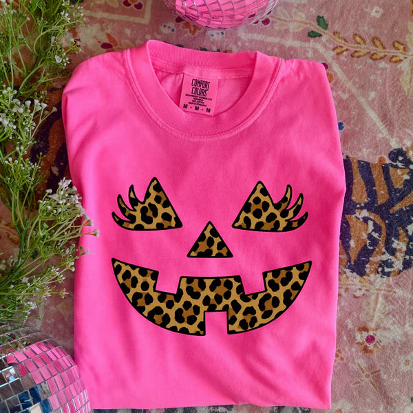 Pink shirt with leopard print pumpkin face design on a patterned surface