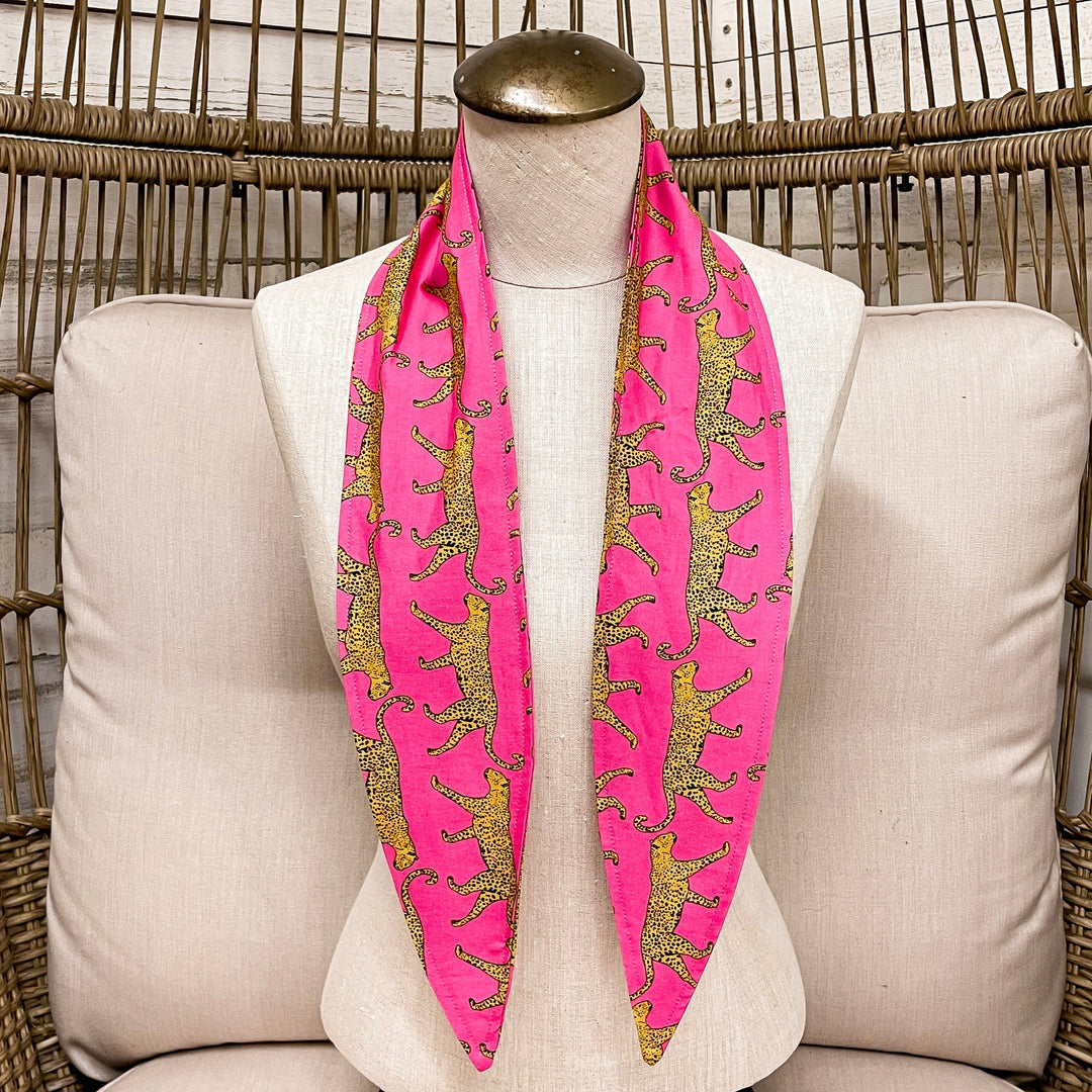 Mannequin wearing a pink scarf with leopards on a white cushioned chair.