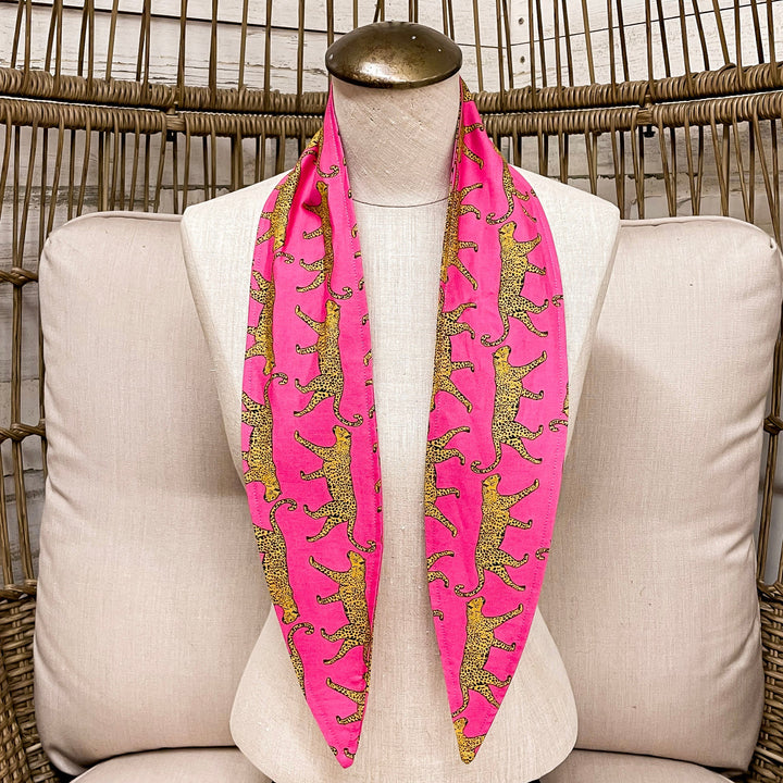 Mannequin wearing a pink scarf with leopards on a white cushioned chair.
