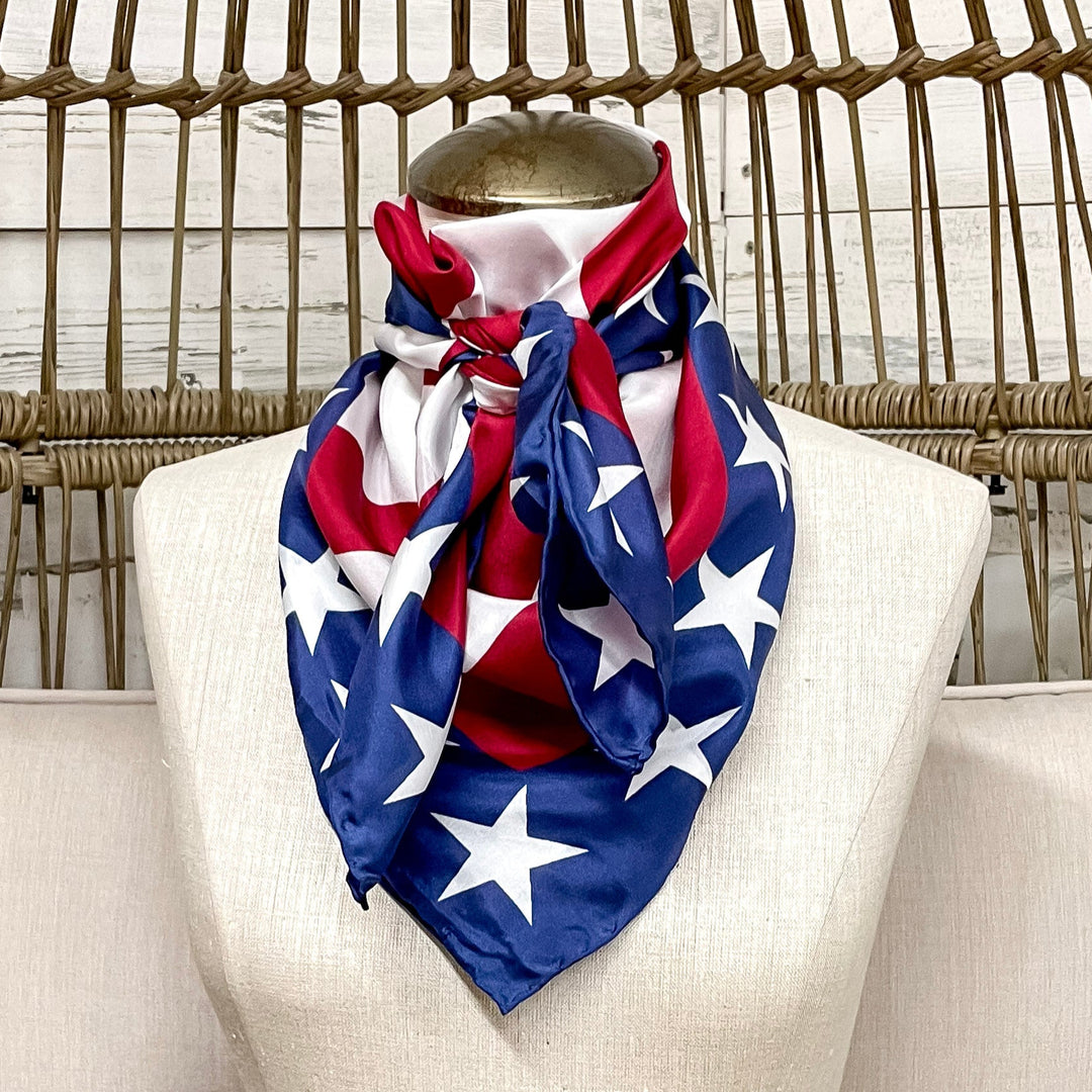 Mannequin wearing a red, white, and blue scarf with a star pattern, sitting on a white cushioned chair.