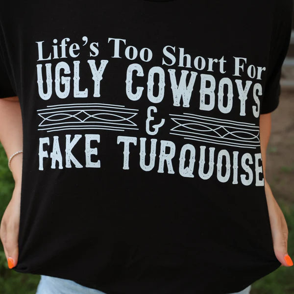 Black t-shirt with white text 'Life's Too Short For Ugly Cowboys & Fake Turquoise' held by a person.
