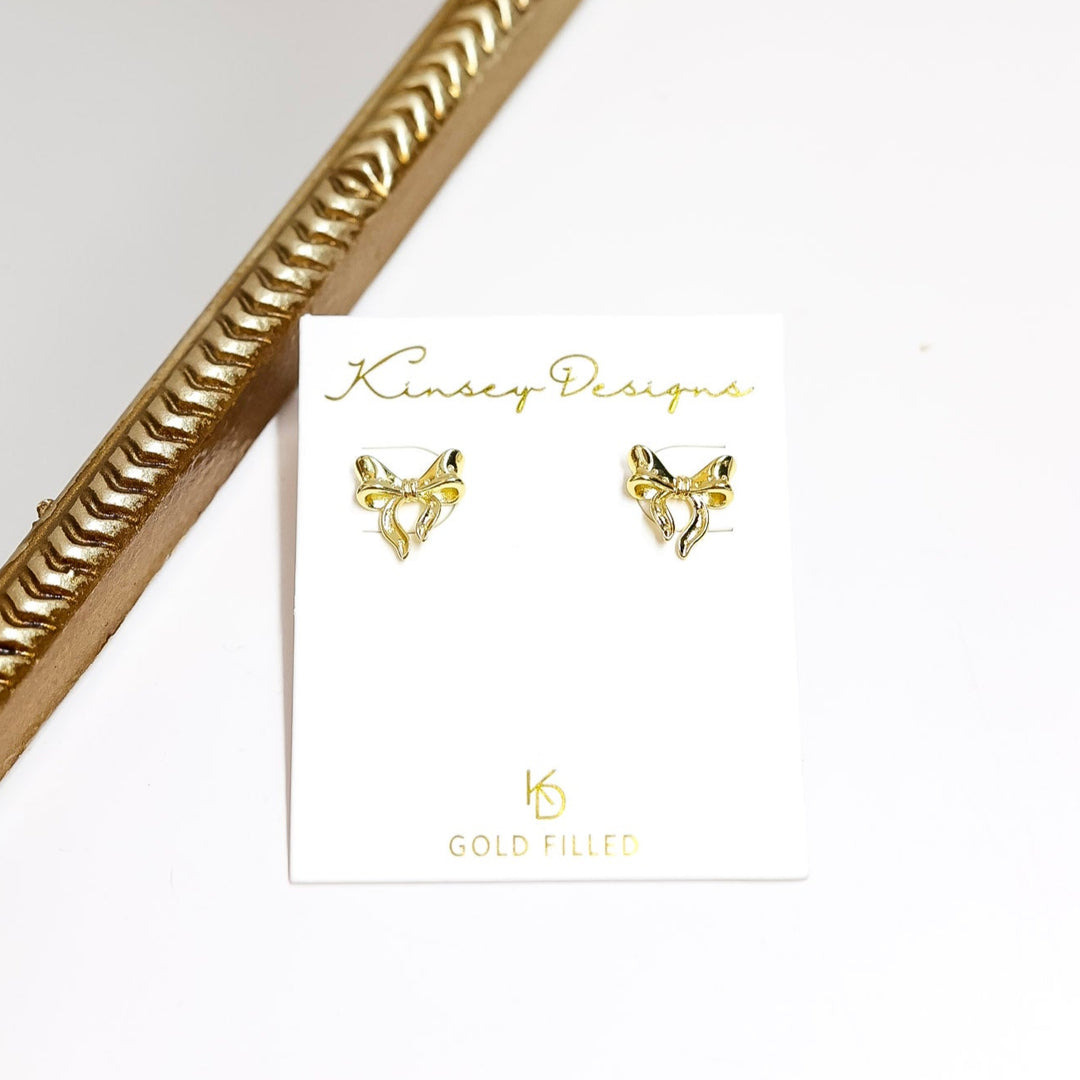 Gold bow earrings on a white card with kinsey designs branding.