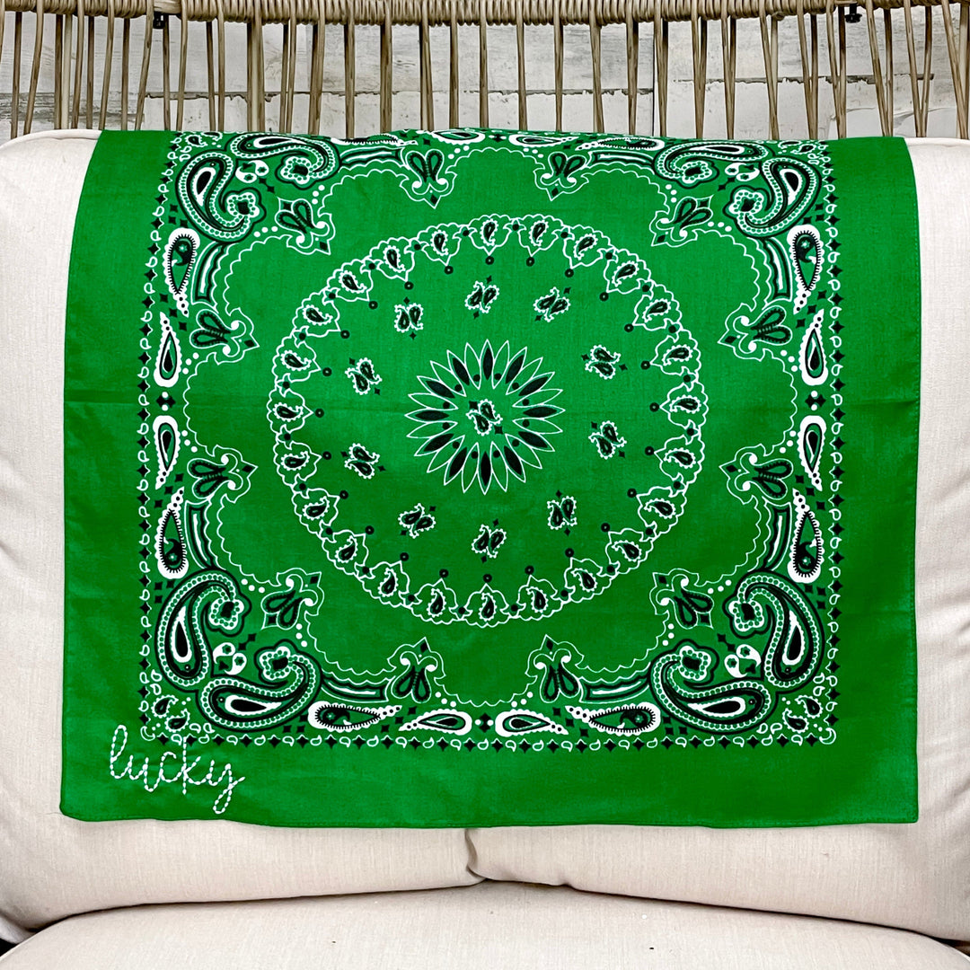 Green bandana with "Lucky" embroidery and white/black patterns on a white cushioned chair.