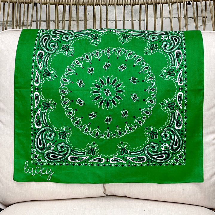 Green bandana with "Lucky" embroidery and white/black patterns on a white cushioned chair.