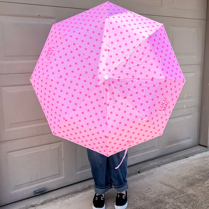 Pink polka-dot umbrella held in front of a garage.
