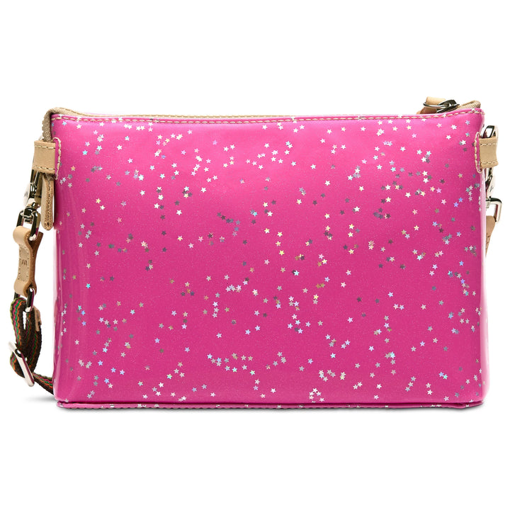 A bright pink crossbody bag with a glossy finish, covered in scattered silver and gold star-shaped glitter, featuring a beige zipper and a matching beige strap with gold hardware.