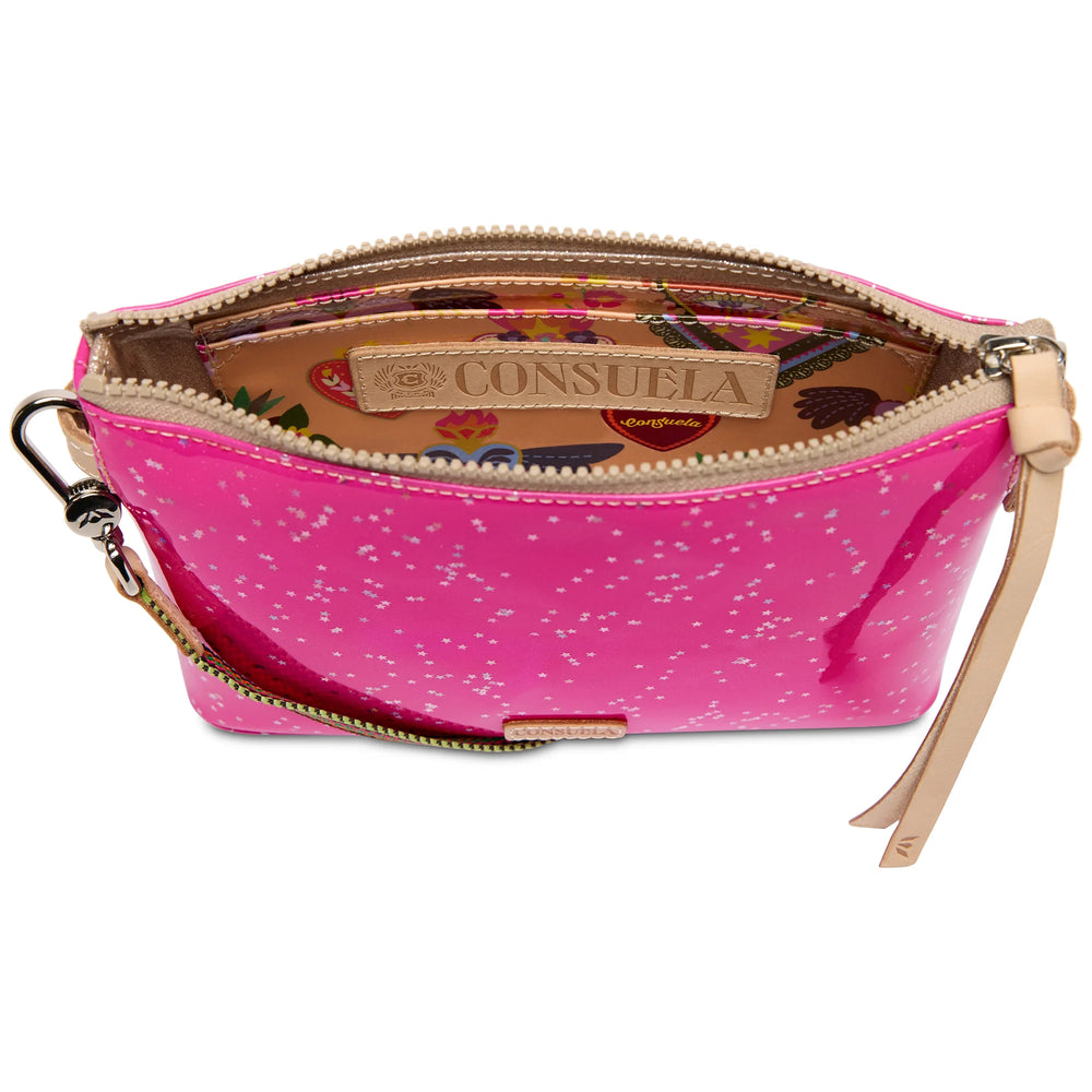 A pink glossy zippered pouch with white speckled pattern, featuring a tan leather interior label that reads 'CONSUELA' and a matching wristlet strap, shown on a white background.
