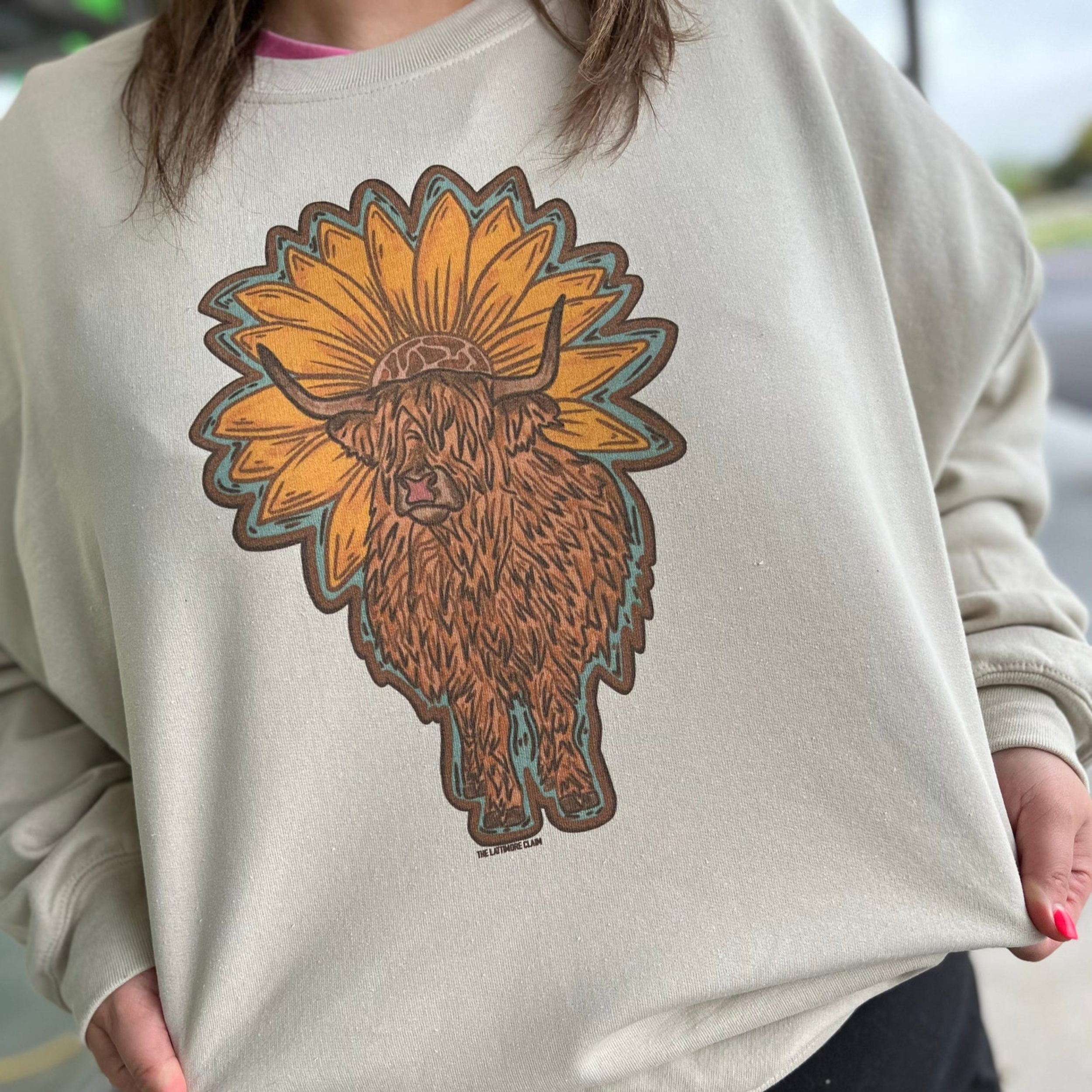 Centered in the picture is a highlander cow infront of a sunflower on a sweater. 