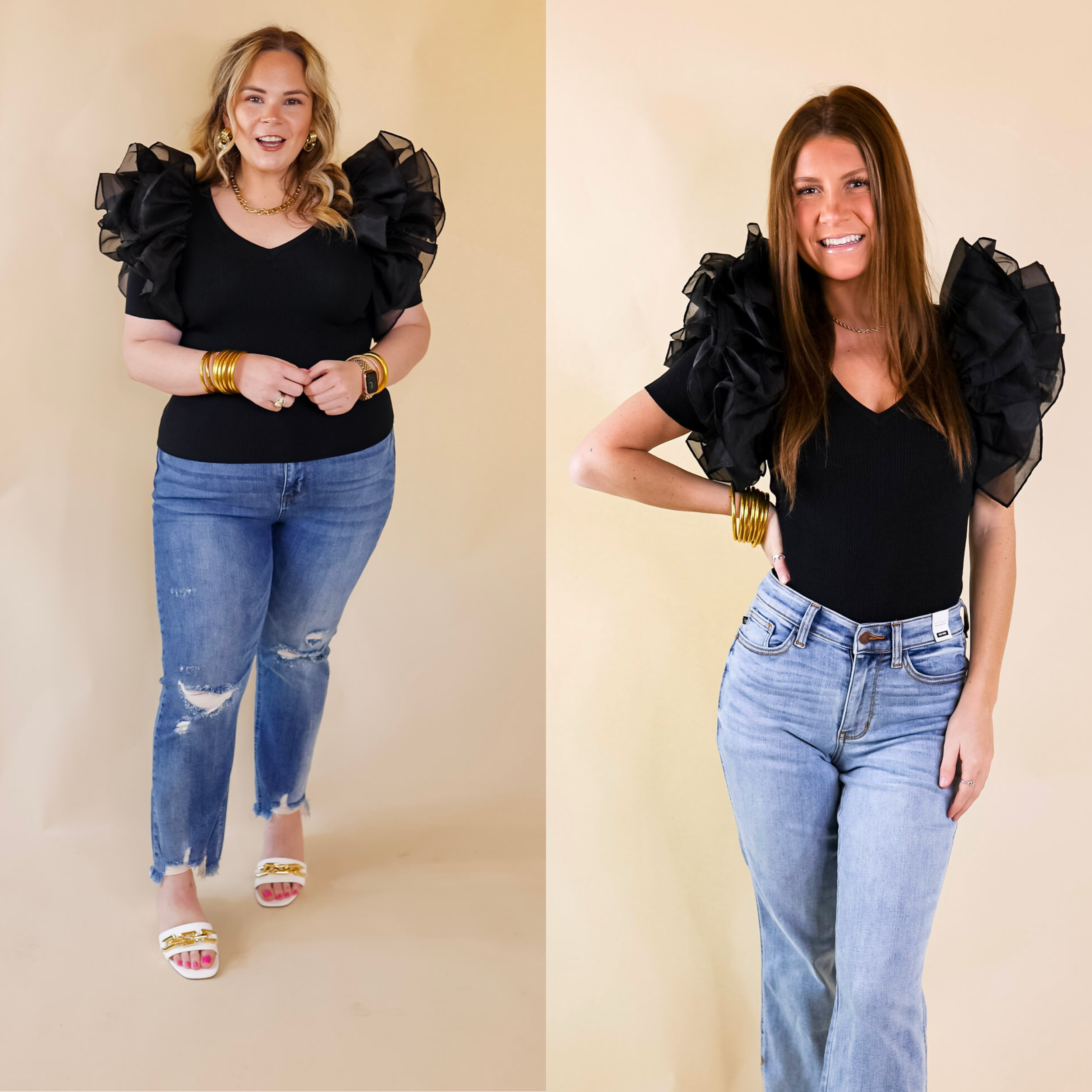 Model is wearing a black fitted top with large ruffle sleeves. Model has this top paired with distressed jeans, white heels, and gold jewelry.