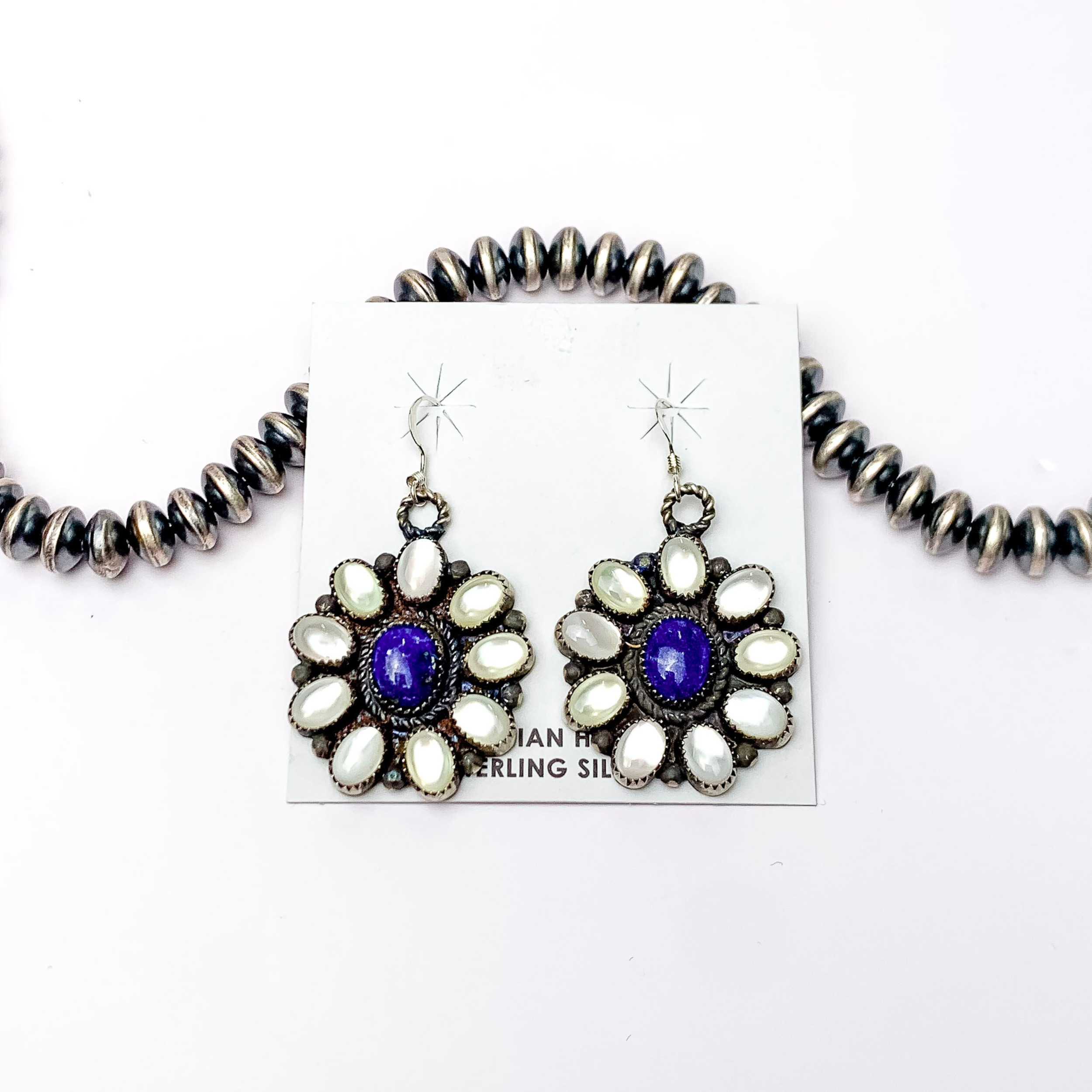 Centered in the picture are sterling silver dangling earrings with a circle cluster of white pearl and Dark lapis center with a white background.  