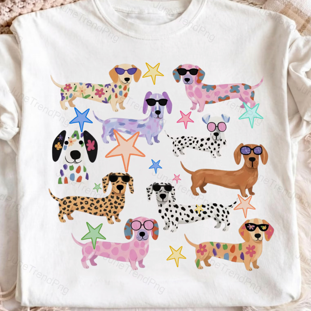 A white t-shirt laid flat, printed with a scattered pack of dachshunds and dalmatians in floral, polka dot, leopard and pastel patterns with sunglasses and stars.